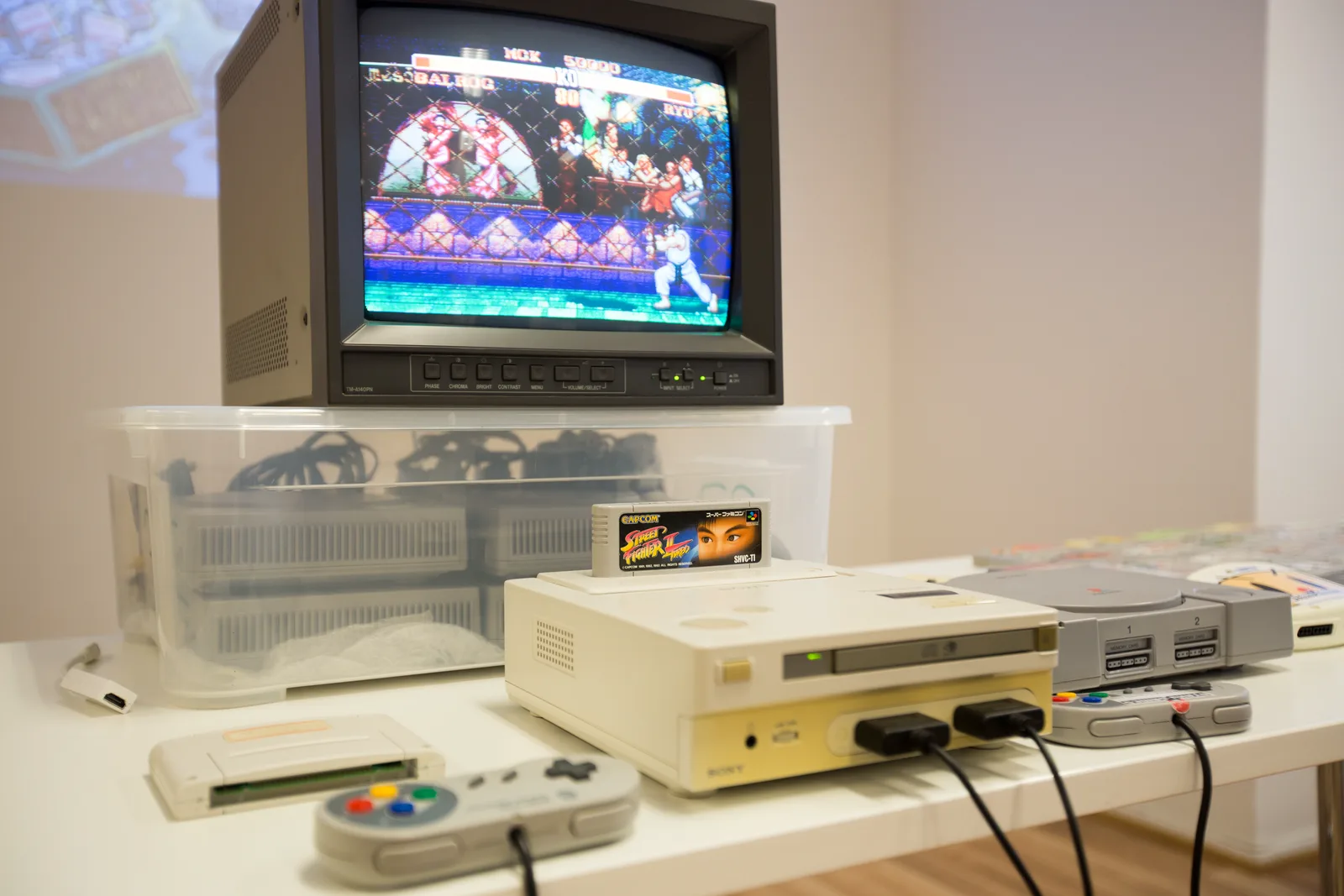 The Nintendo PlayStation prototype console on a table with a Super Famicom cartridge on top and a monitor behind it.