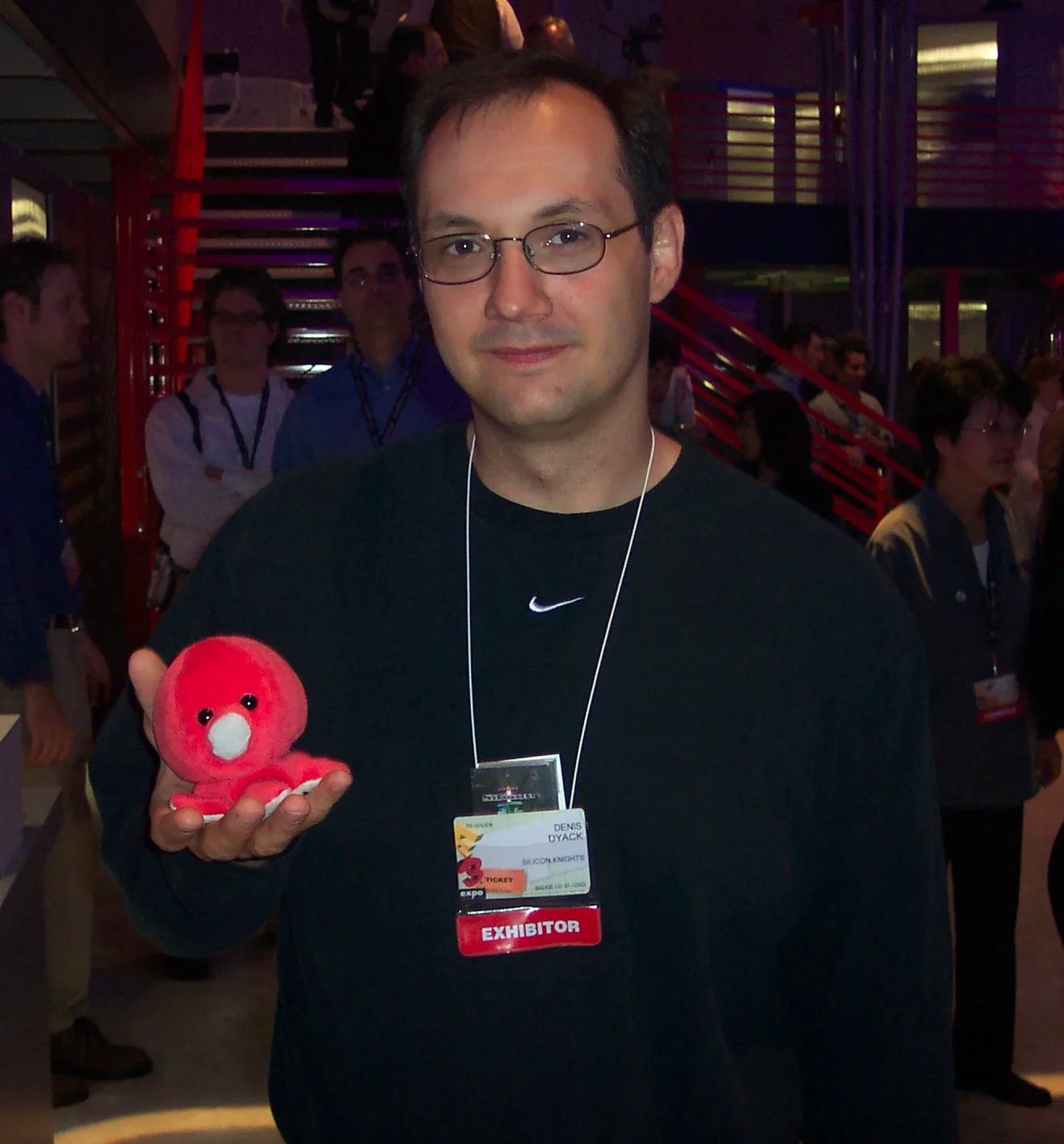 Denis Dyack holding a small red plush octopus, wearing an E3 Expo exhibitor badge from Silicon Knights
