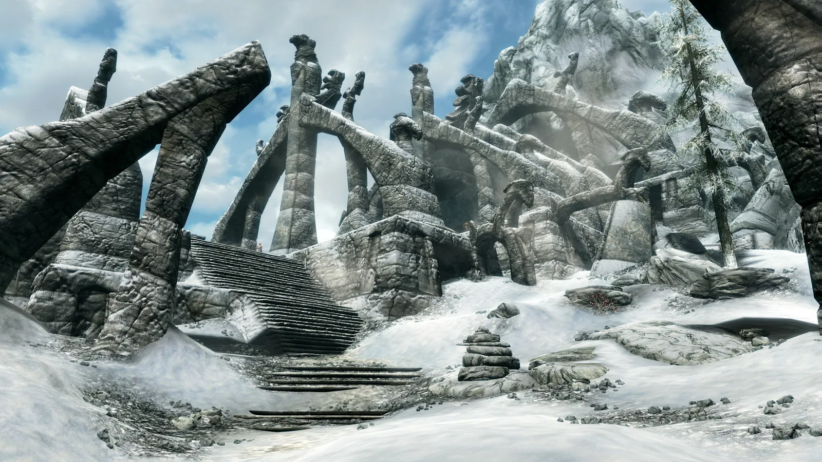 Snow-covered ancient stone ruins with carved arches and steps under a cloudy sky in Skyrim Special Edition