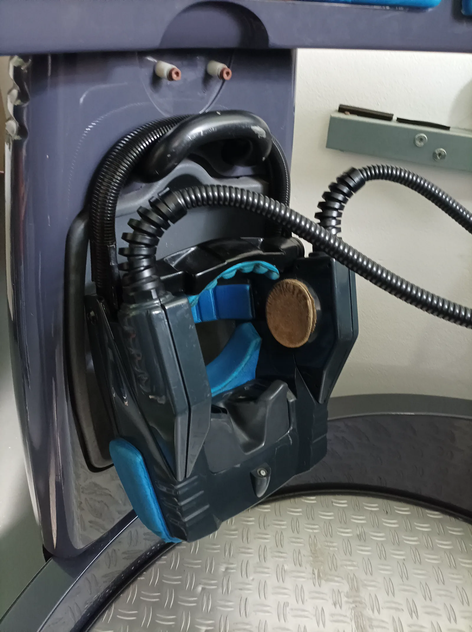 A dark Virtuality headset with blue padding and a thick ribbed cable, hanging on the side of a 1000CS pod.